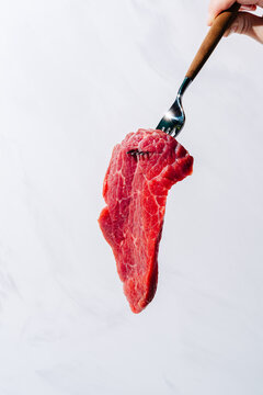 Raw beef flap steak on a fork against a white backdrop