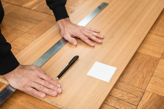 Closeup photo of male joiner measuring and marking wooden board Marking plywood sheet on floor for renovation and installation work