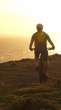 Man on a mountain bike rides along a coastal path during a beautiful sunset over the ocean