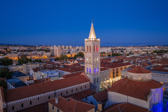 Aerial view of the illuminated bell tower of St. Anastasia Cathedral rising high above the terracotta rooftops, casting a warm glow over the historic city, Zadar, Zadar County, Croatia.