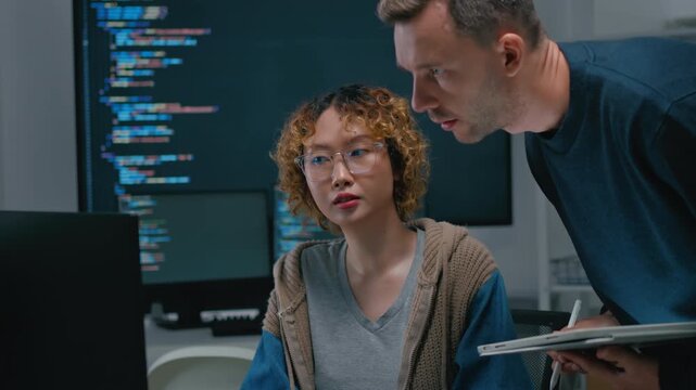 Focused diverse software engineers and AI developers working on code on computer screens in a dark office. Concept of machine learning, digital transformation, and future technology innovation.