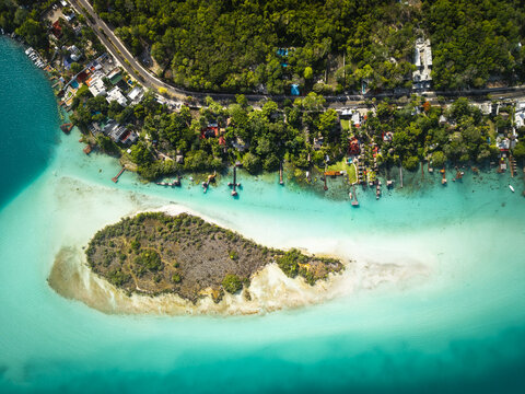 Aerial view of the vibrant turquoise waters surrounding a small island near the lush green shoreline, creating a striking contrast in color and texture, Bacalar, Quintana Roo, Mexico.