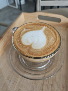 Delightful cup of latte art coffee with heart foam on wooden tray creates warm romantic valentine mood while verticle view captures cozy cafe beverage morning happiness breakfast