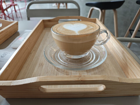 Romantic valentine hot latte art coffee cup on wooden tray with white heart foam showing love and passion in cozy cafe atmosphere for verticle morning breakfast beverage concept