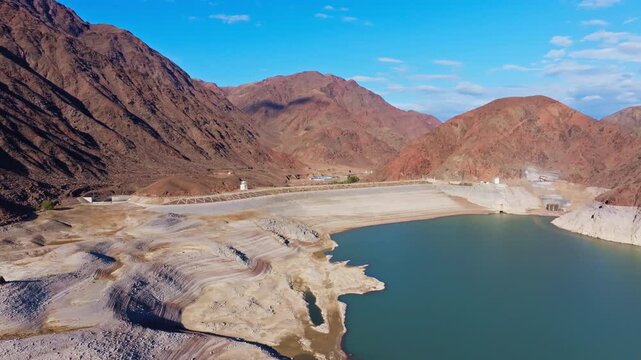 Aerial view captures expansive dam and tranquil Orto Tokoy reservoir amidst arid mountains in autumnal Kyrgyzstan.