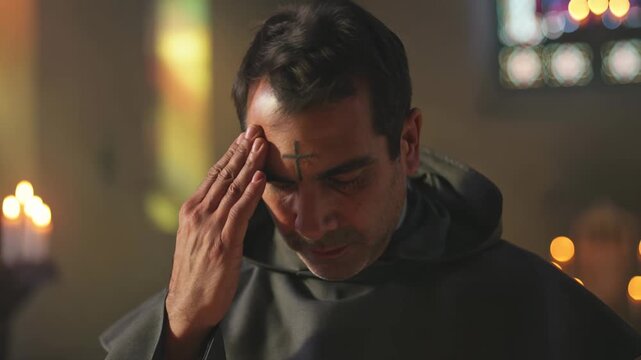 Christian monk with ash cross on forehead praying in church with candlelight, lent christian devotion.