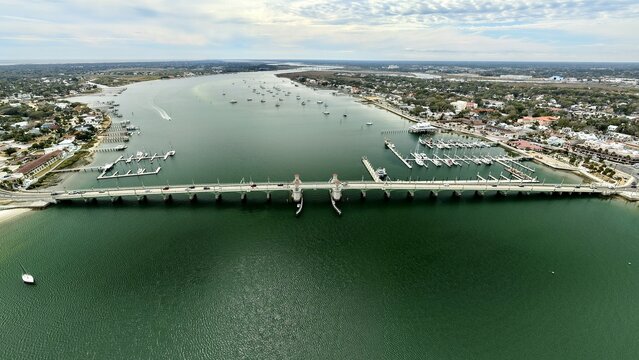 Aerial view of the vibrant green water reflecting the sky under the bridge, with boats docked on either side, St. Augustine, Florida, United States.