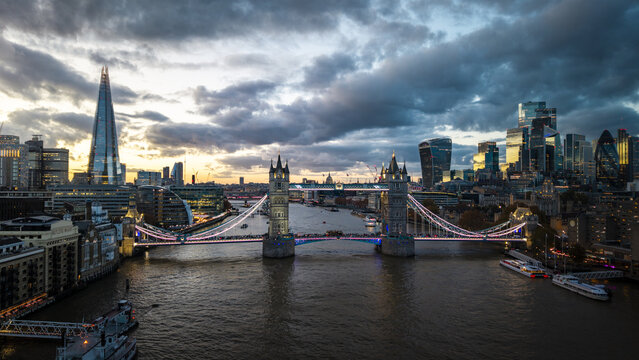 Aerial view of Tower Bridge illuminated against the twilight, with the Shard and city skyscrapers piercing the skyline, London, United Kingdom.