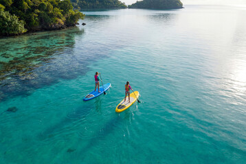 Two women paddle in calm water on a SUP board. Aerial drone footage.