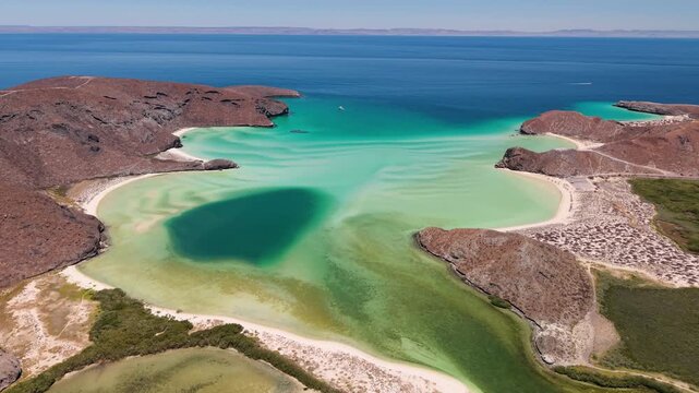 Aerial view of stunning turquoise waters meeting the sandy shores of Balandra Beach, framed by rugged, arid cliffs, La Paz, Baja California Sur, Mexico.