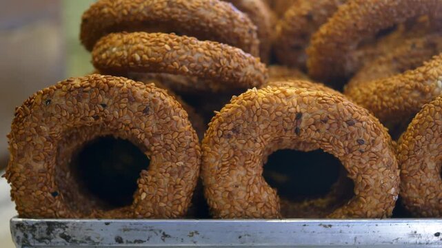 Close up of many sesame bagels stacked on a metal tray in natural light
