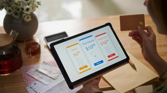 Cropped shot of unrecognizable person paying for service subscription with credit card using digital tablet while sitting at table with utility bills and paychecks