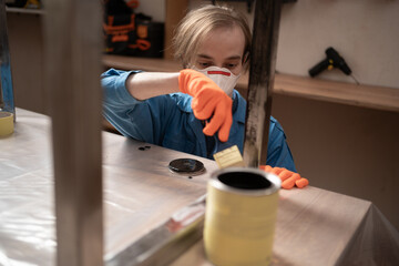 Male worker in overalls and protective mask painting metal construction for furniture in garage or small workshop