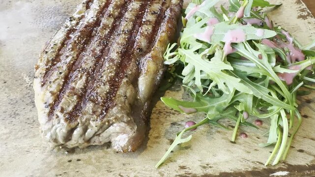 A close-up of a grilled steak. The meat sits on a wooden board with arugula leaves nearby. A cafe menu.