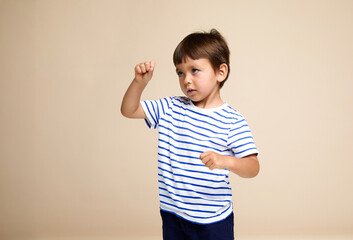 Profile portrait of a little boy in a striped t-shirt, posing in the studio, islated a beige background. © Corina