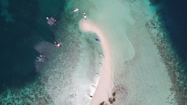Aerial view of several boats floating on clear turquoise waters near a white sandbar, contrasting with the dark blue sea, Coron, Mimaropa, Philippines.
