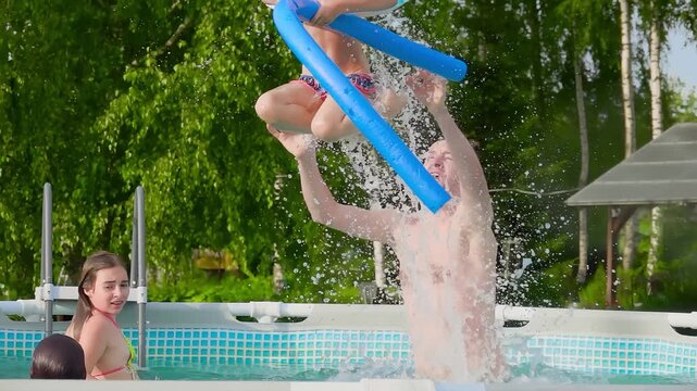 Happy father throwing little daughter up in swimming pool at country house. Summer family vacation, water splashes and healthy lifestyle concept.