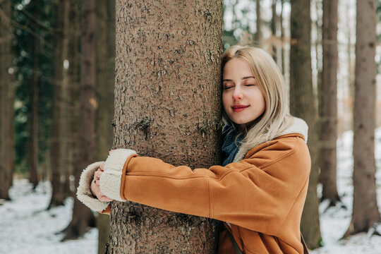 Woman hugging pine tree in snowy forest enjoying nature and relaxation