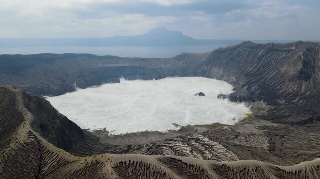 Aerial view of the Taal Volcano's crater lake, its white water contrasts sharply with the dark, rocky terrain, Taal Lake, Calabarzon, Philippines.