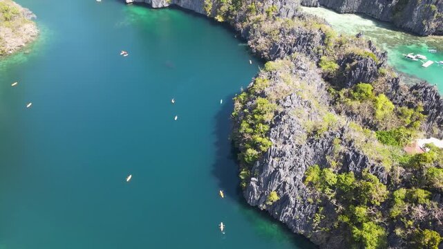 Aerial view of boats and kayaks sailing on turquoise water near islands with black rock formations and green trees, El Nido, Mimaropa, Philippines.