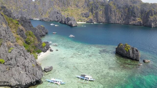Aerial view of boats sailing on turquoise waters surrounded by majestic limestone cliffs and lush green vegetation, El Nido, Mimaropa, Philippines.