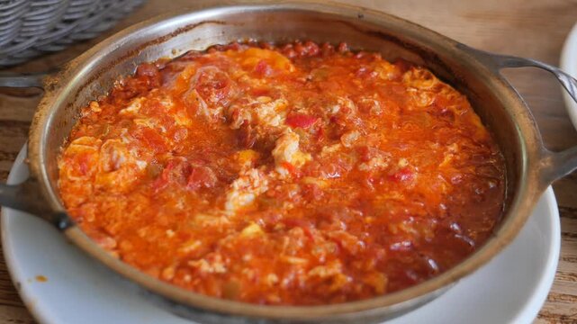 Close up of traditional turkish menemen eggs with tomato and peppers in copper pan on wooden table