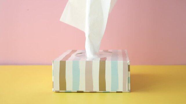 Soft white tissue gently pulled from striped box on yellow and pink background