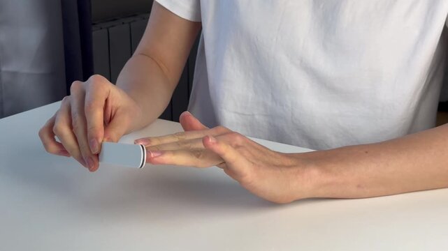 A European woman sits at a table and files her nails. Home beauty treatments. Self-care. Medium shot. Home manicure.