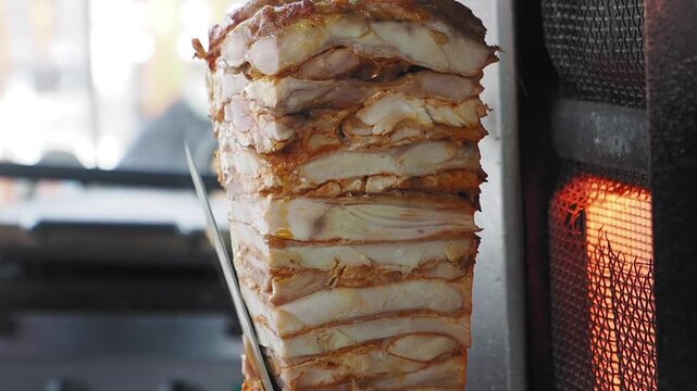 Chef cutting traditional turkish chicken doner kebab on vertical spit for shawarma wrap preparation