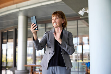 Businesswoman in a business suit smiles while holding a smartphone and making a video call in the office