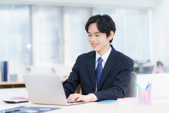 オフィスでノートパソコンで仕事をするスーツを着た若い日本人男性