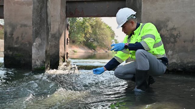 A water resources officer is collecting water samples near a sluice gate for quality testing