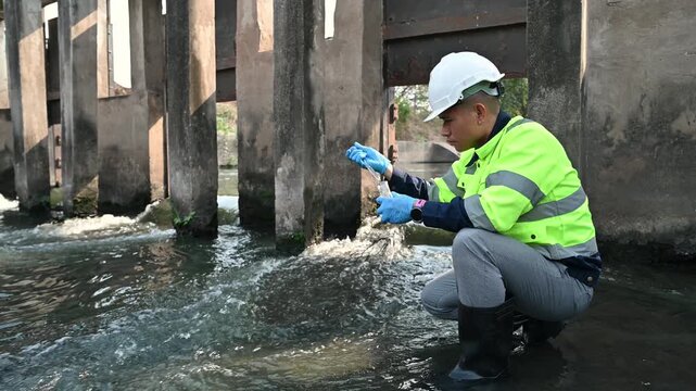 A water resources officer is collecting water samples near a sluice gate for quality testing