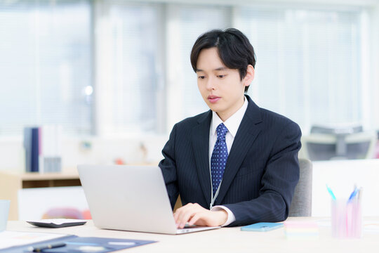 オフィスでノートパソコンで仕事をする困った顔のスーツを着た若い日本人男性