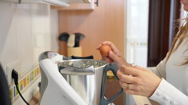 A woman is cooking in a kitchen with a blender on the counter. She is wearing a white shirt and has a ring on her finger