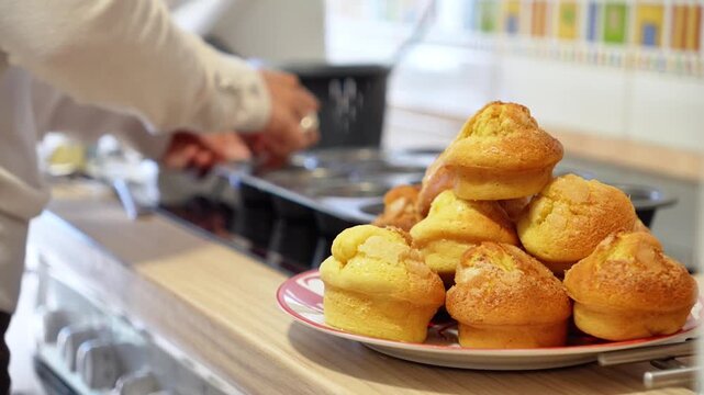 A person is cooking muffins on a stove. The muffins are on a plate and are piled up