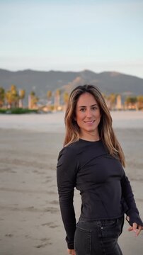 A woman is running on a beach with mountains in the background. She is smiling and she is enjoying herself