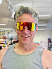 Smiling middle aged man wearing colorful sports sunglasses indoors