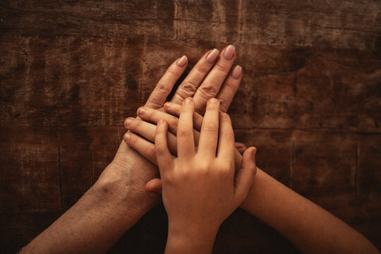 Hands of different ages and skin tones placed together on a wooden surface, symbolizing connection and unity among generations in a warm, natural setting