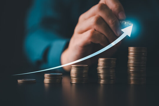 Business hand stacking coins in rising columns with glowing arrow graph symbolizing smart investment financial growth and digital economy success