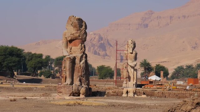 Colossi of Memnon monumental sculptures in West Bank Luxor Egypt, two seated pharaoh statues with hieroglyphic details and mountain landscape background