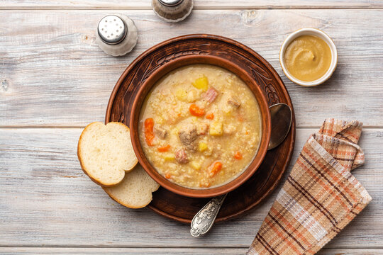 Soup kulesh with millet, potatoes, onion, carrot, meat and bacon in ceramic bowl on wooden background.