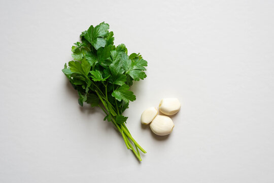 Ramillete de perejil y tres dientes de ajo sobre fondo blanco. 