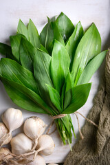 Fototapeta premium Fresh wild garlic leaves with garlic bulbs arranged on white rustic background. Natural green foliage highlights seasonal foraged food. Flat lay, top view