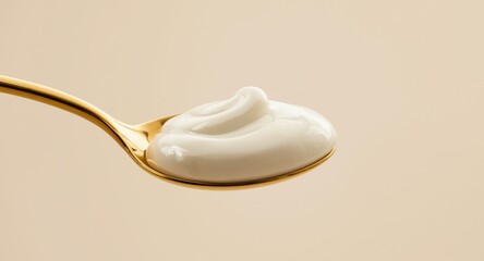 Shiny golden spoon filled with silky dairy yogurt isolated on plain background
