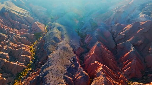 Aerial view captures dramatic eroded sandstone rock formations and serene valleys in Kyrgyzstan. Majestic mountainous terrain showcases natural beauty under sunset daylight.