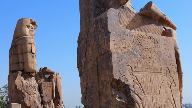 Colossi of Memnon massive royal statues from 14th century BC in Luxor Egypt, weathered sandstone sculptures of seated pharaoh with preserved lower sections