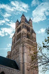 Fotobehang Brugge portrait shot of old ancient medieval building in bruges brugge in belgium with trees and leaves coming into frame and cloudy blue clear skies above in autumn   © STJMEDIA