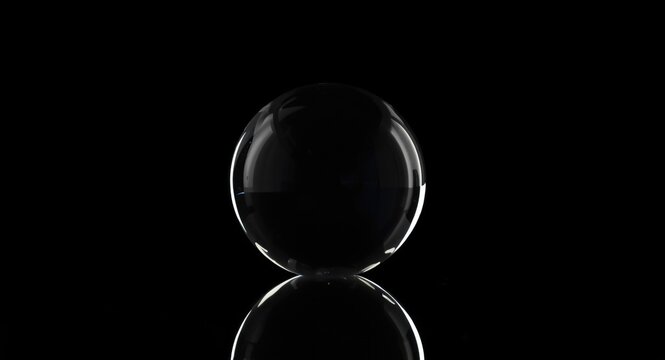 Glass sphere sitting on polished reflective surface including copy space and solid black background