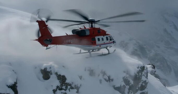 Red helicopter flying over snowy mountains with rotor blades spinning